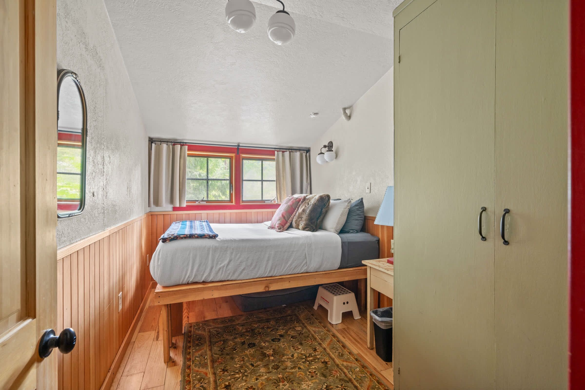 A room with a bed, a window, a wardrobe, and a small stool.