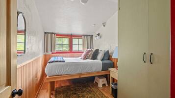 A room with a bed, a window, a wardrobe, and a small stool.
