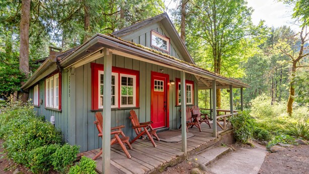 A rustic cabin with a porch, wooden chairs, and a red door. - Riverfront Retreat - Mt Hood Views, Sleeps 4! (Mount Hood Village)