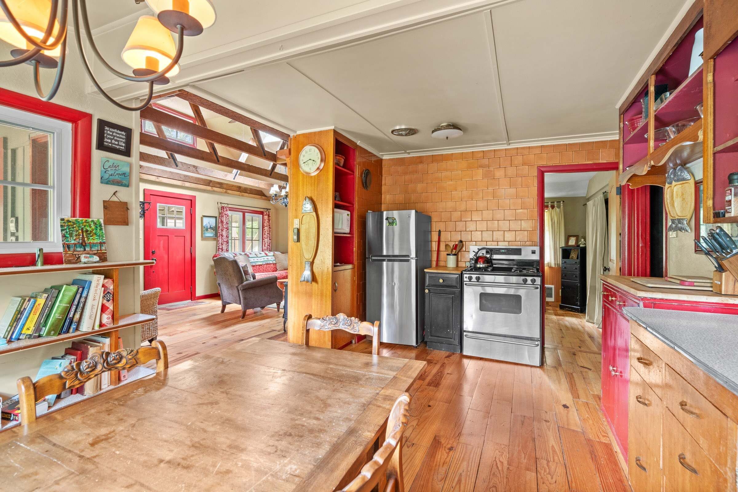 A cozy kitchen with wooden flooring, a dining table, and a red door.