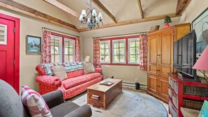 A cozy living room with a red sofa, a wooden coffee table, and a television on a wooden cabinet. - Riverfront Retreat - Mt Hood Views, Sleeps 4! (Mount Hood Village)