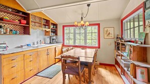 A kitchen with wooden cabinets, a dining table, and chairs. There is a window with a view of greenery outside. - Riverfront Retreat - Mt Hood Views, Sleeps 4! (Mount Hood Village)