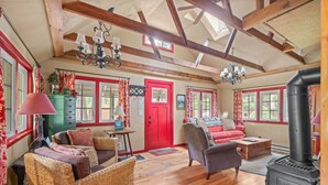 A cozy room with a red door, wicker furniture, a fireplace, and a wooden ceiling. - Riverfront Retreat - Mt Hood Views, Sleeps 4! (Mount Hood Village)