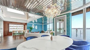 A modern interior with a round marble table, blue upholstered chairs, a decorative chandelier, and a view of the water through large windows. - Aqua Star - Iconic Floating Home, Seen on HGTV (Portland)