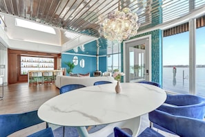 A modern interior with a round marble table, blue upholstered chairs, a decorative chandelier, and a view of the water through large windows. - Aqua Star - Iconic Floating Home, Seen on HGTV (Portland)