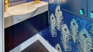 A bathroom with a peacock feather pattern on the walls, a gold-framed mirror, and a white sink. - Aqua Star - Iconic Floating Home, Seen on HGTV (Portland)