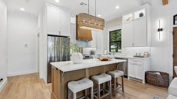 A modern kitchen with a central island, bar stools, a stainless steel refrigerator, and a hanging light fixture.