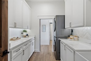 A modern kitchen with white cabinetry, a stainless steel refrigerator, and a wooden countertop.