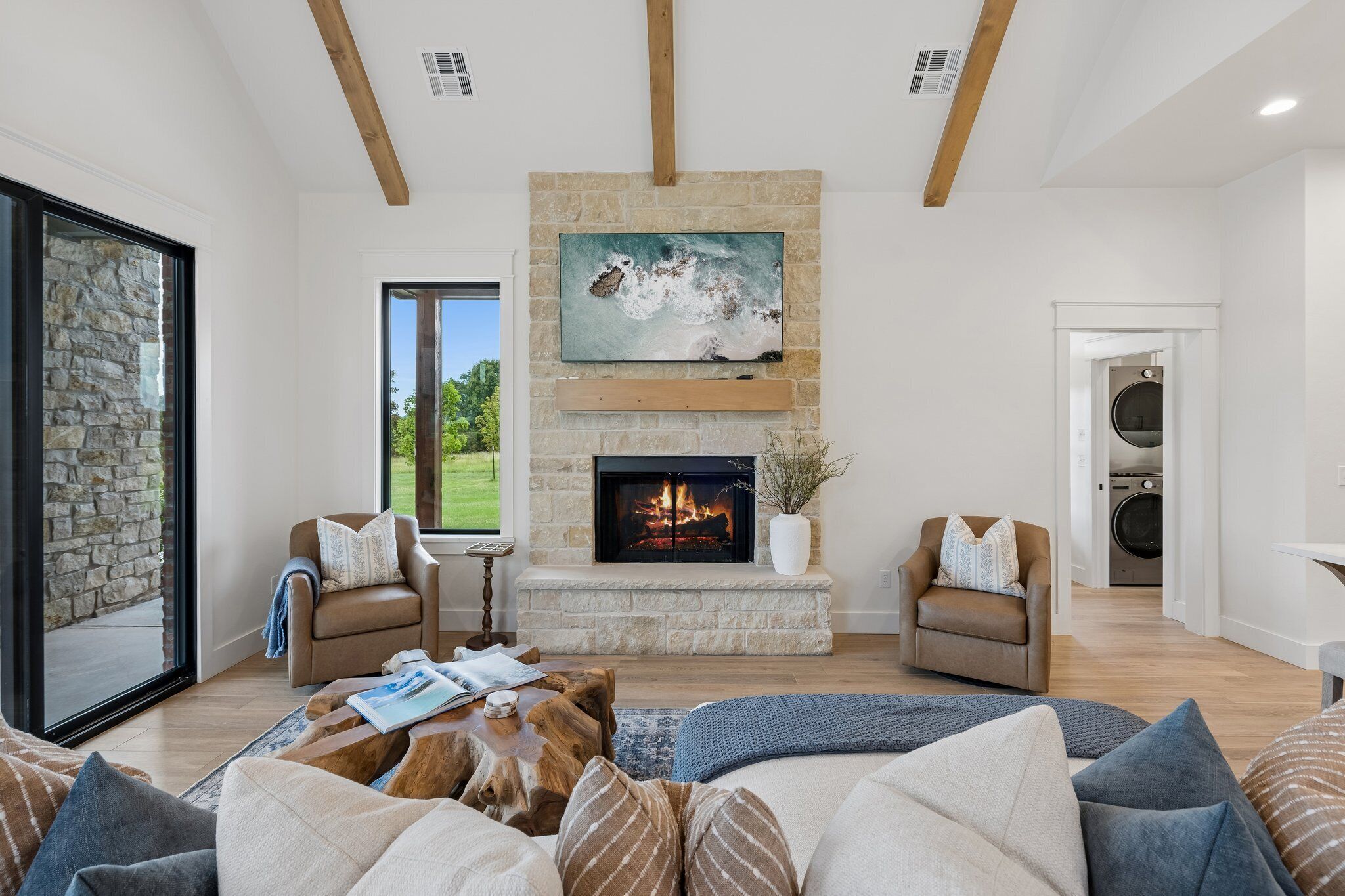 A spacious living room with a fireplace, stone fireplace surround, and a large window overlooking a garden.