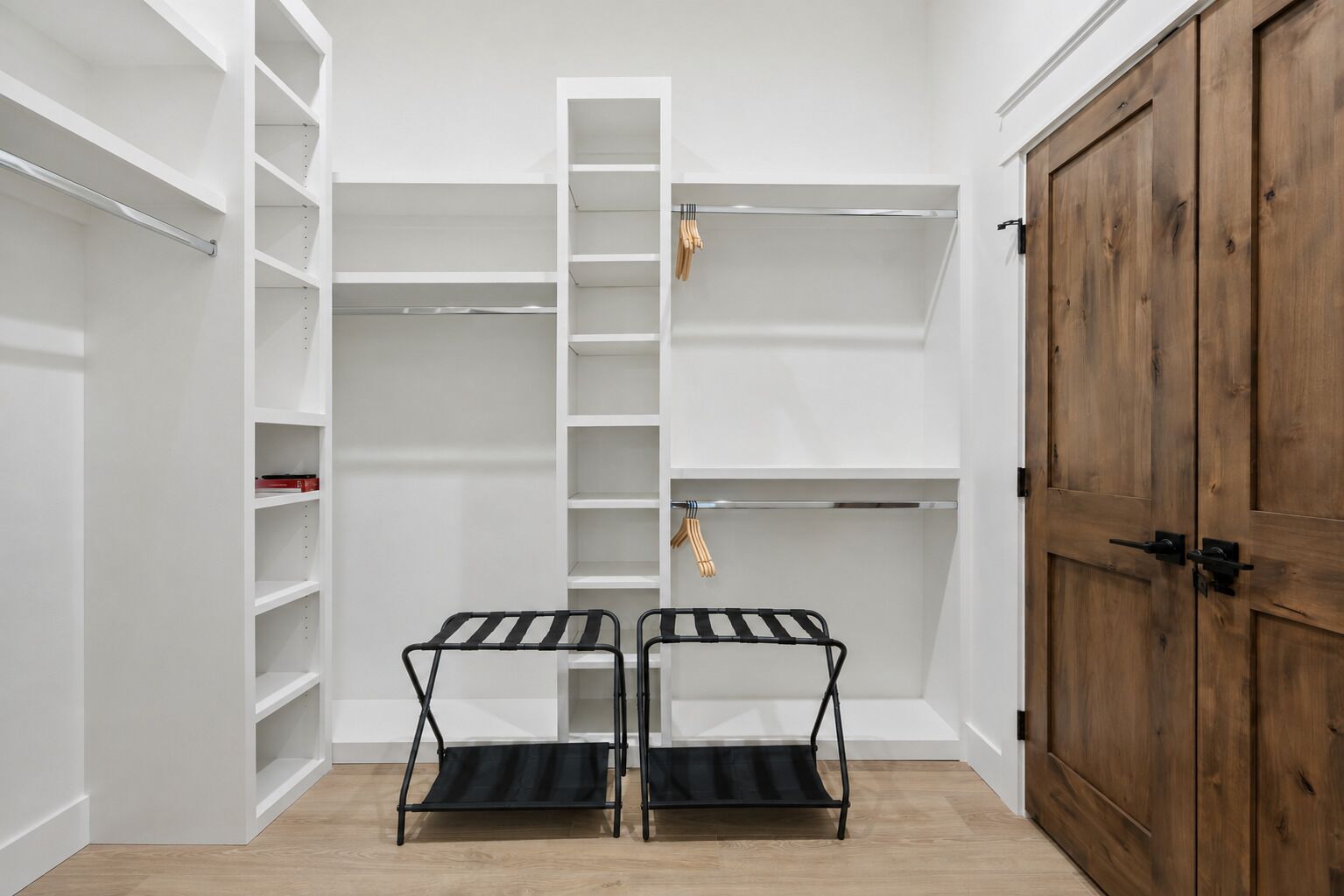 A walk-in closet with open shelves, a wooden wardrobe, and two black metal drying racks.