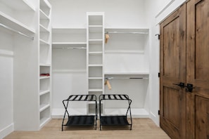 A walk-in closet with open shelves, a wooden wardrobe, and two black metal drying racks.