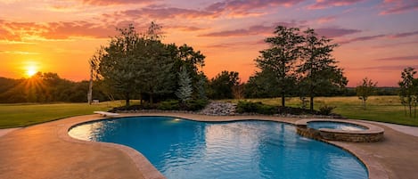 A swimming pool with a curved design, surrounded by a stone border and a landscaped area with trees.