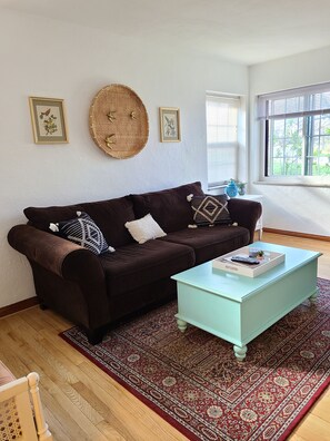 A living room with a brown sofa, a light blue coffee table, a patterned rug, and framed artwork on the wall. - A Travel Nurse's Cozy Bird's Nest 1B1B Apartment (St. Louis)