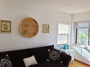 Ein Zimmer mit einem braunen Sofa, zwei gerahmten Bildern, einem Wandteppich und einem Fenster mit Jalousien.
