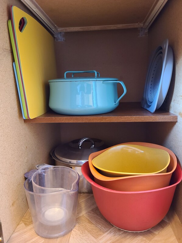Uma prateleira na cozinha com uma panela azul, tigelas amarelas e vermelhas, e um recipiente medidor transparente.