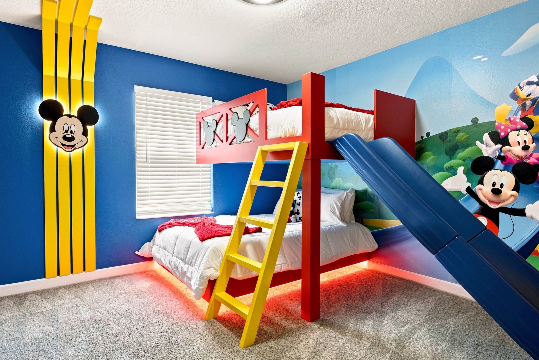 Een kinderkamer met een stapelbed, een ladder, een Mickey Mouse decoratie aan de muur en een muurschildering van Disney-personages.