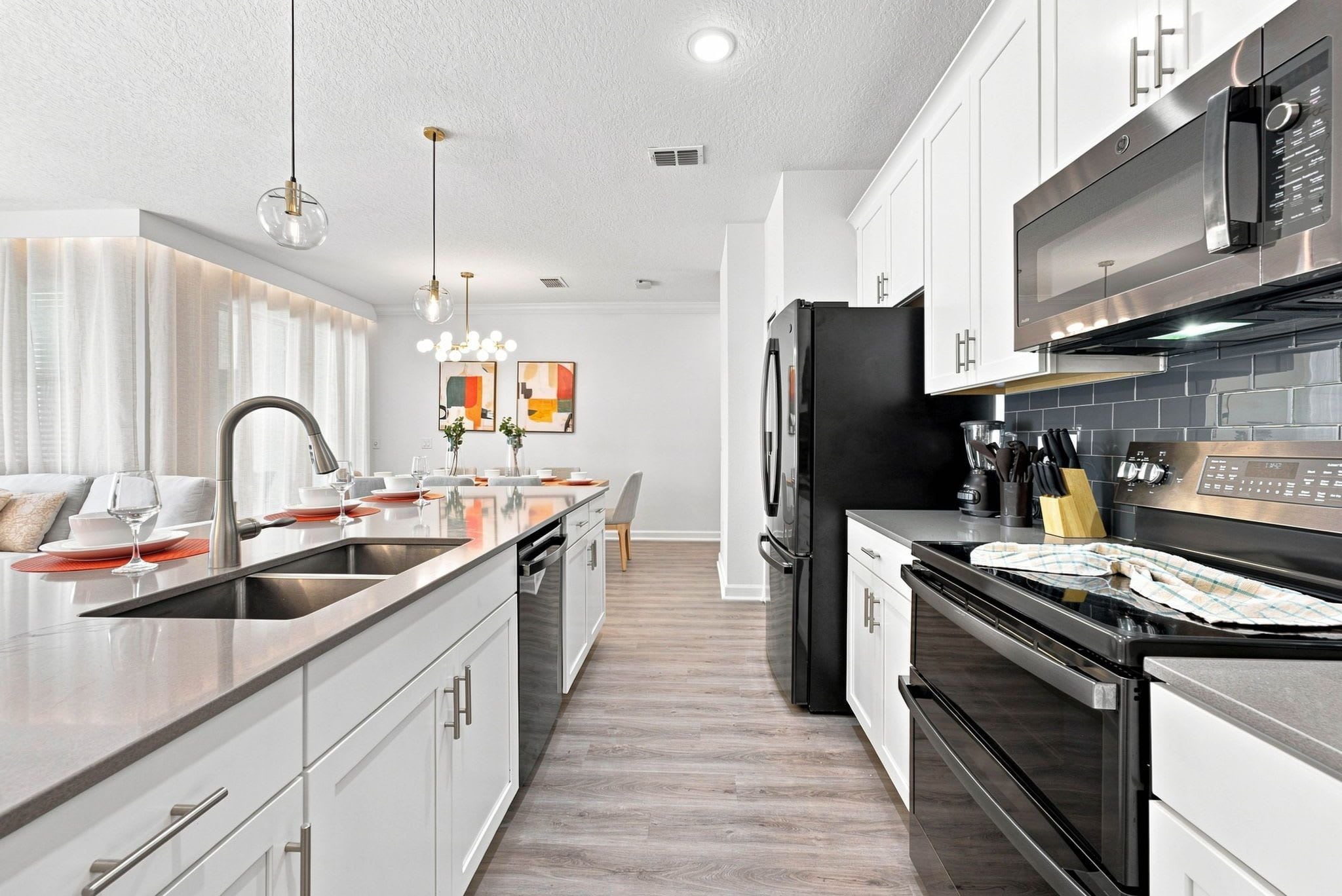 A modern kitchen with a central island, stainless steel appliances, and a dining area with a view to the living room.