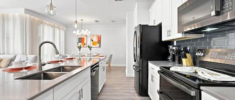 A modern kitchen with a central island, stainless steel appliances, and a dining area with a view to the living room.