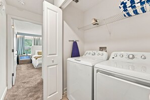 A laundry room with two white washing machines, a drying rack, and a towel hanging on the wall. - Chic Disney Retreat with Fun Themed Rooms (Kissimmee)