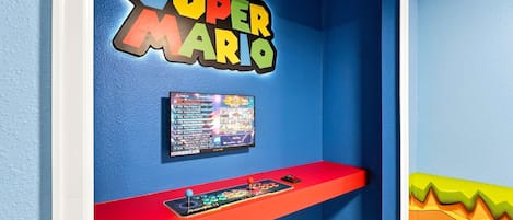 Habitación con pared azul, un cartel de Super Mario, una consola de videojuegos y un estante con cartuchos de juego.