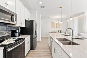 A modern kitchen with stainless steel appliances, a central island, and pendant lighting. - Chic Disney Retreat with Fun Themed Rooms (Kissimmee)