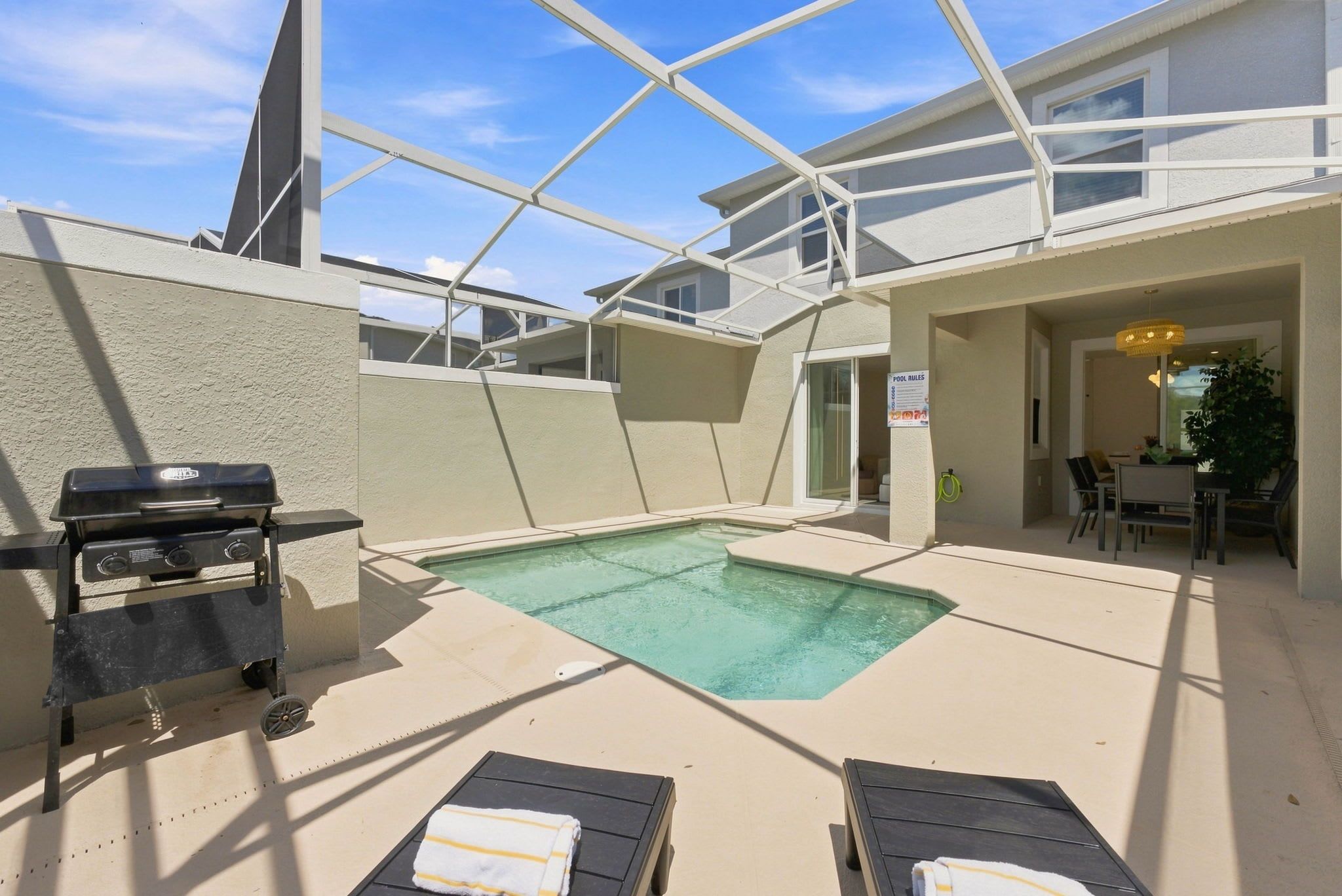 A pool area with a grill, lounge chairs, and a covered patio.
