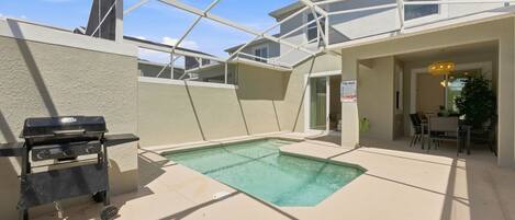 A pool area with a grill, lounge chairs, and a covered patio.