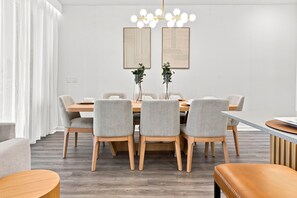 A modern dining area with a round table, six grey upholstered chairs, a wooden floor, and a chandelier with multiple light bulbs. - Chic Disney Escape, Themed Rooms & Private Pool (Four Corners)