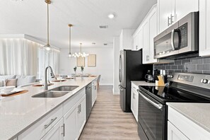 A modern kitchen with stainless steel appliances, white cabinetry, and pendant lighting. - Chic Disney Escape, Themed Rooms & Private Pool (Four Corners)