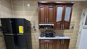 Une cuisine avec un réfrigérateur noir, des armoires en bois, un four à micro-ondes et un plan de travail.