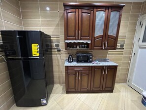 A kitchen with a black refrigerator, wooden cabinets, a microwave, and a countertop. - Luxurious Apartment - Gardenia Nasr City (Cairo)
