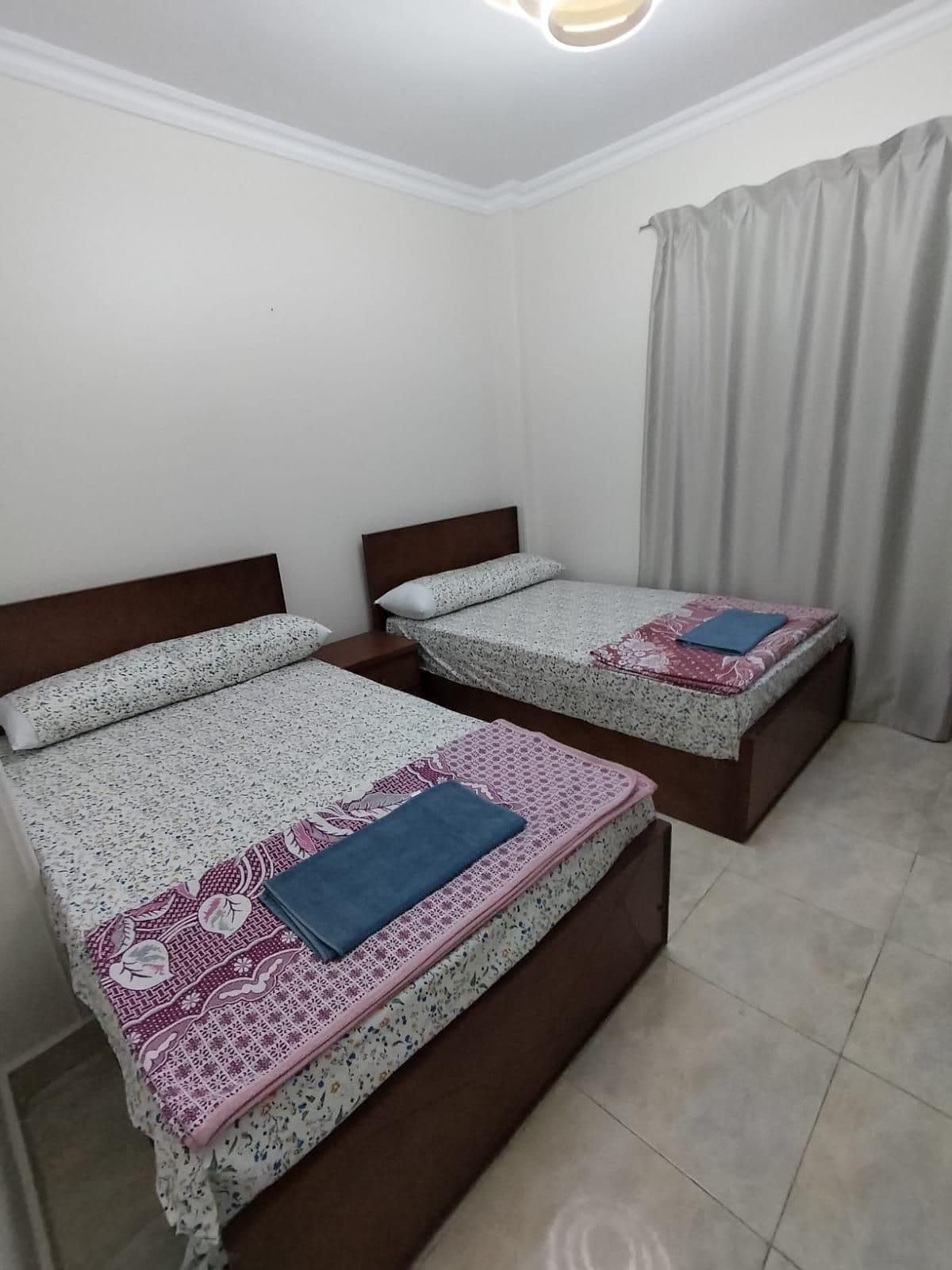 A hotel room with two beds, each with a wooden headboard, a patterned bedspread, and a blue blanket.