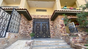 Une entrée d’immeuble agrémentée d’un portail en métal décoratif, un escalier menant à une porte et une petite plante en pot.