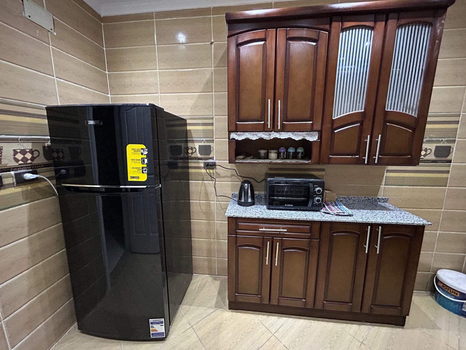 Eine kleine Küche mit einem schwarzen Kühlschrank, einer Mikrowelle und Holzschränken.