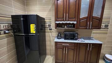Een kleine keuken met een zwarte koelkast, een magnetron en houten kastjes.