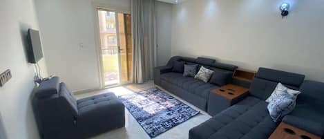 A modern living room with a sofa set, a flat-screen TV, and a sliding glass door to the outside.