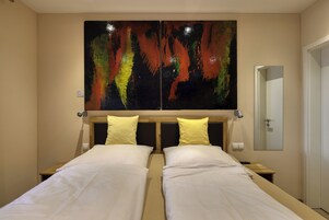 A hotel room with two beds, a large abstract painting above, and a door to the right.