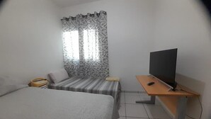 A bedroom with a bed, a desk with a television, and a window with patterned curtains.
