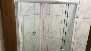 Eine gläserne Duschkabine mit weißer Tür, gefliesten Wänden und einem sichtbaren Abfluss.