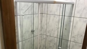 Eine gläserne Duschkabine mit weißer Tür, gefliesten Wänden und einem sichtbaren Abfluss.