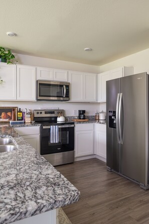 A modern kitchen with white cabinets, a stainless steel refrigerator, a microwave, and a stove.