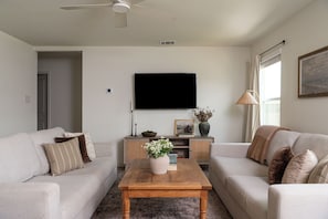 A living room with two sofas, a coffee table, a flat-screen TV, a lamp, and a painting on the wall.