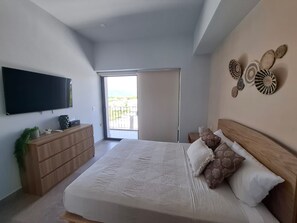 A bedroom with a bed, a dresser, a television, and a balcony. - Nuevo Vallarta apartment with pool (Las Jarretaderas)