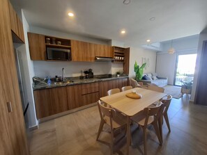 A modern kitchen with wooden cabinets, a built-in microwave, and a dining area with a table and chairs. - Nuevo Vallarta apartment with pool (Las Jarretaderas)