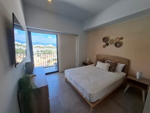 Ein Schlafzimmer mit einem großen Bett, einem Nachttisch, einem Beistelltisch, einem an der Wand befestigten Fernseher und einem Balkon mit Blick auf die Stadt.