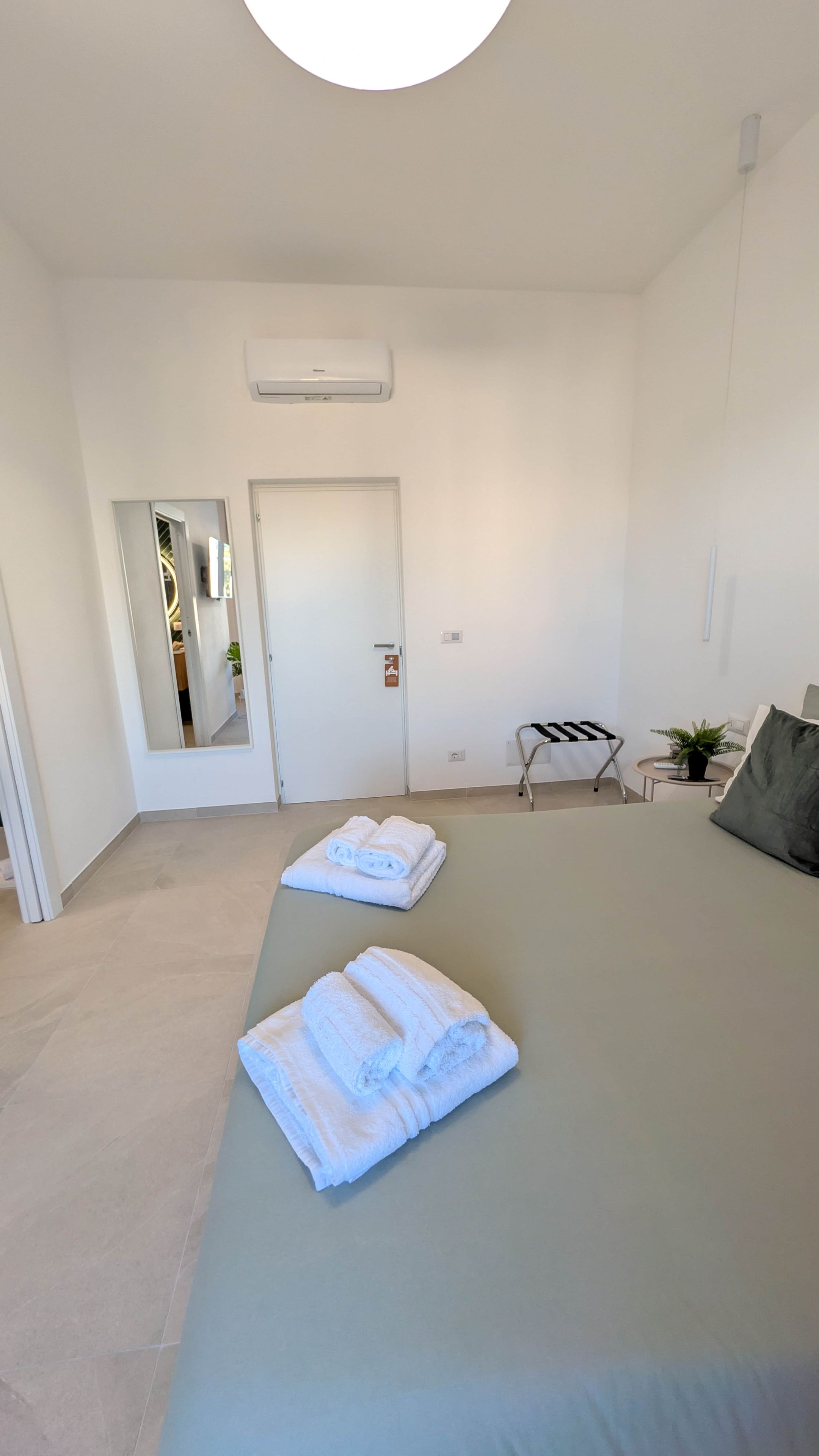 Habitación de hotel con cama, espejo, puerta y una mesita con una planta.