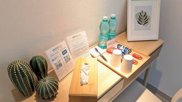 Un escritorio de madera con una planta enmarcada, un calendario, un dispensador de pañuelos, un bolígrafo, una botella de agua y una bandeja con aperitivos.