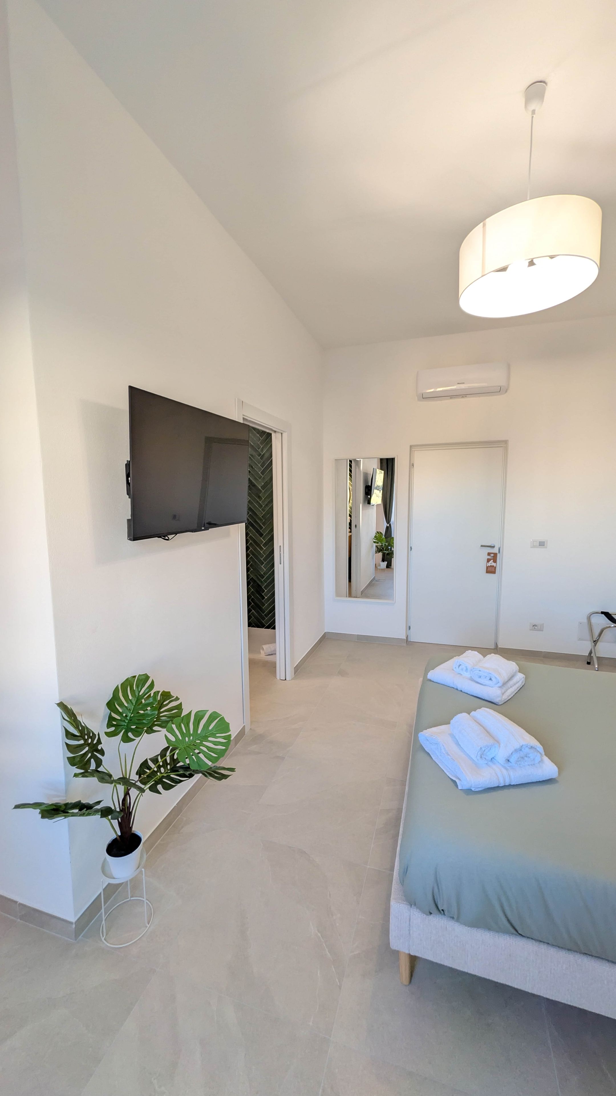 A modern bedroom with a bed, a TV mounted on the wall, a potted plant, and a hallway leading to another room.