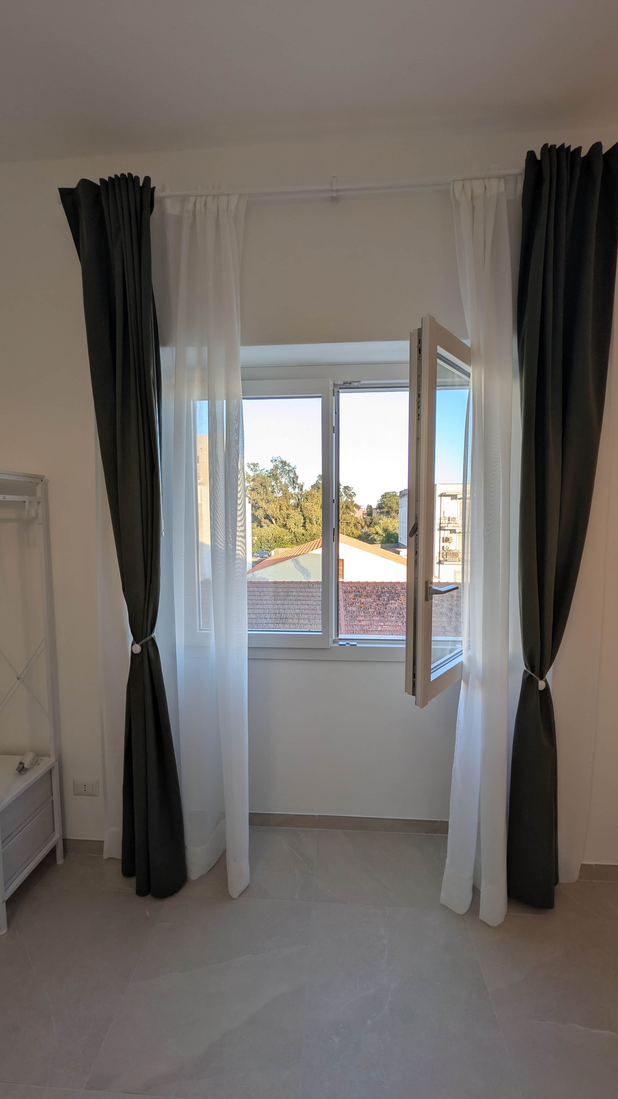 A room with a large window, white walls, and a tiled floor.