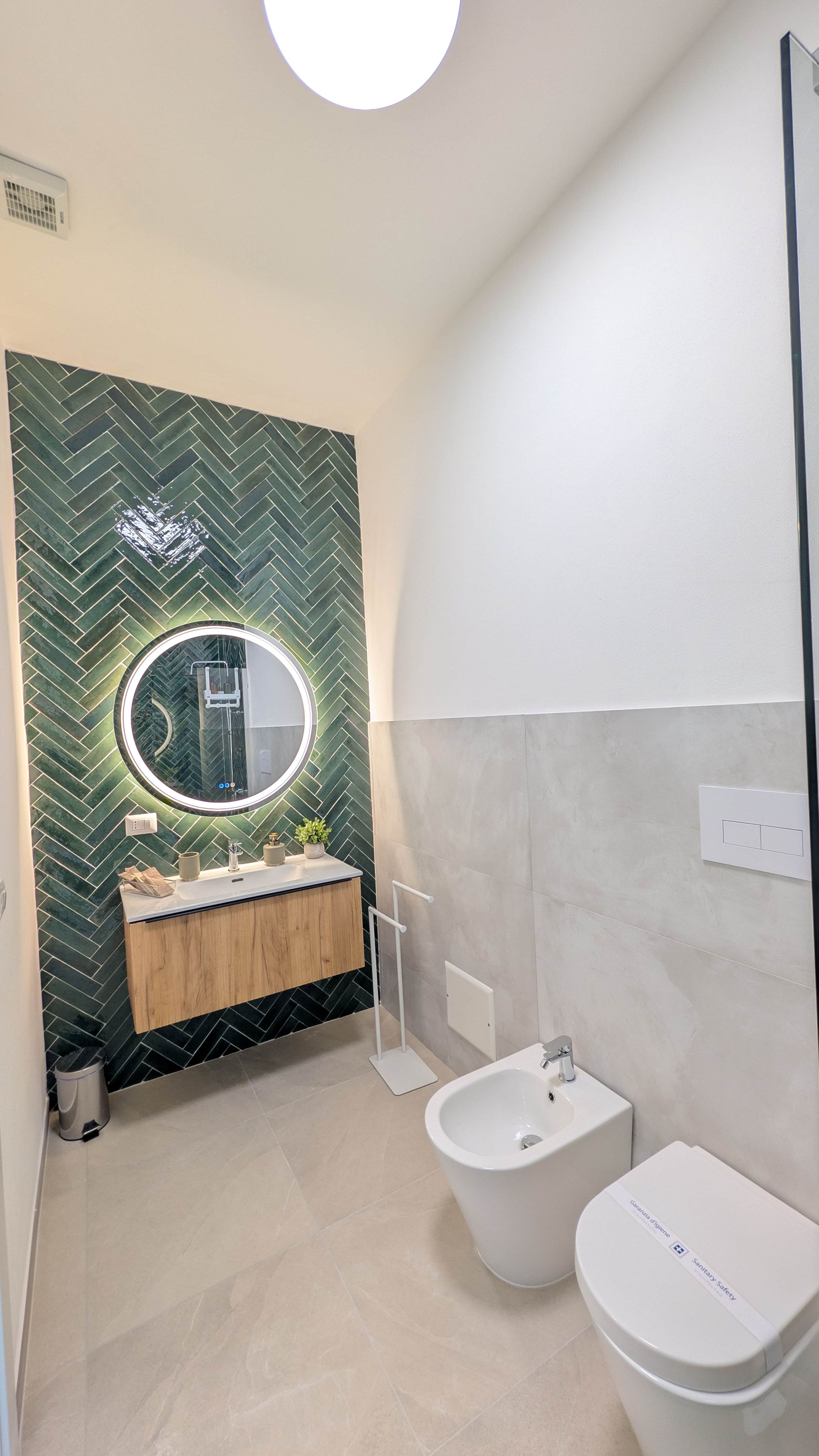 Ein modernes Badezimmer mit einem Zinkmuster-Rückwand, einem runden Spiegel, einem Holzausleger und einem Bidet sowie einer Toilette.